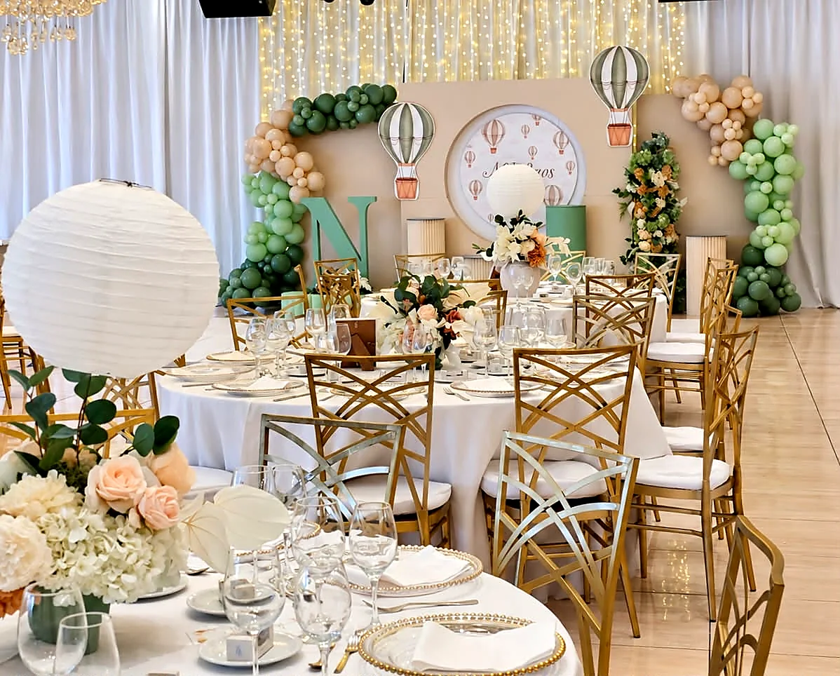 Christening tables in a ballroom with paper lanterns, sage balloons and gold chairs