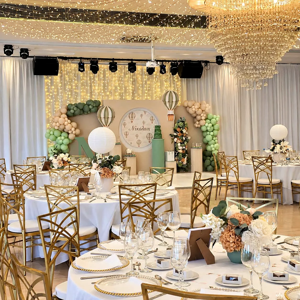 Christening tables in a ballroom with sage green details, gold chairs and a fairy-light ceiling