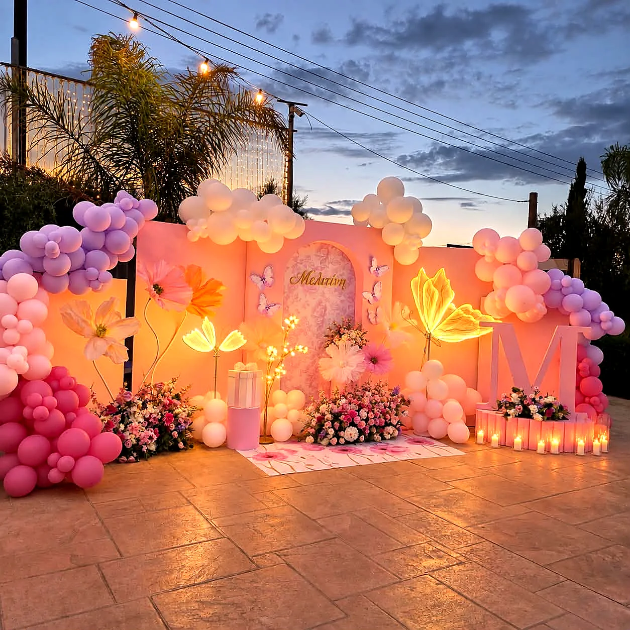 A pink butterfly christening backdrop lit at dusk with balloon garlands and candles