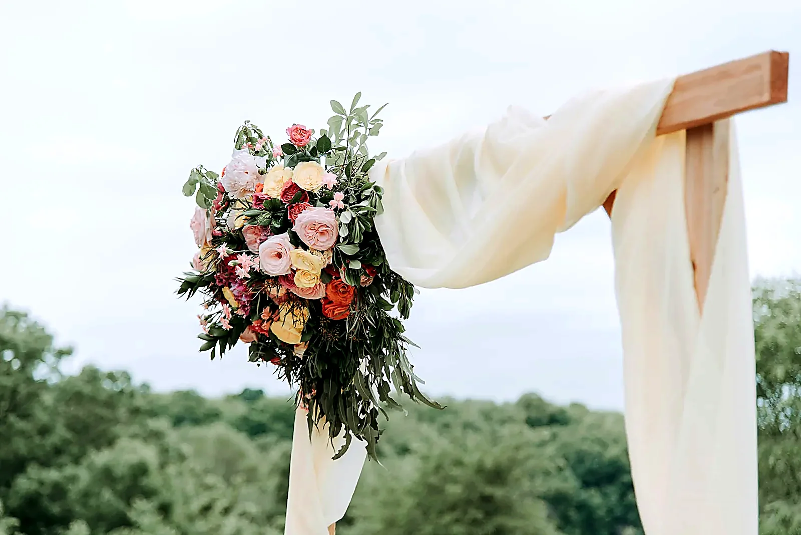 A wooden ceremony arch dressed with soft ivory drapery and a blush and green floral corner