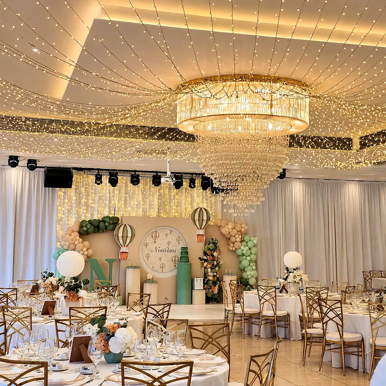 A wide view of a ballroom with a fairy-light ceiling, crystal chandeliers and laid banquet tables