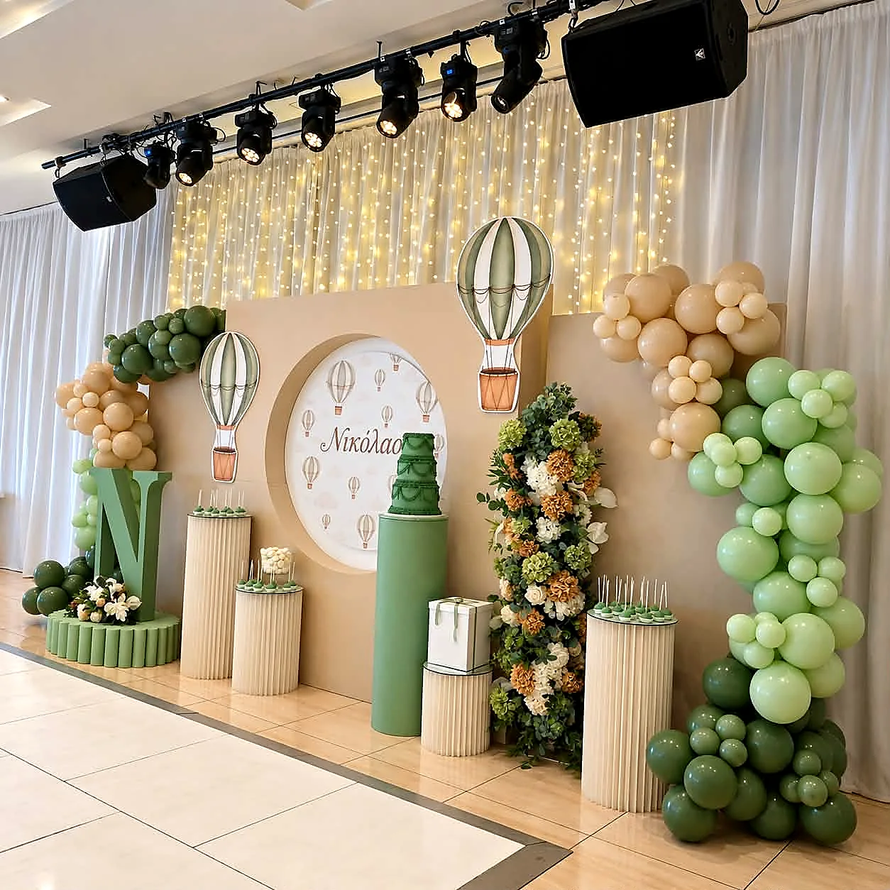 A christening backdrop in sage green and cream with hot-air-balloon motifs and balloon garlands