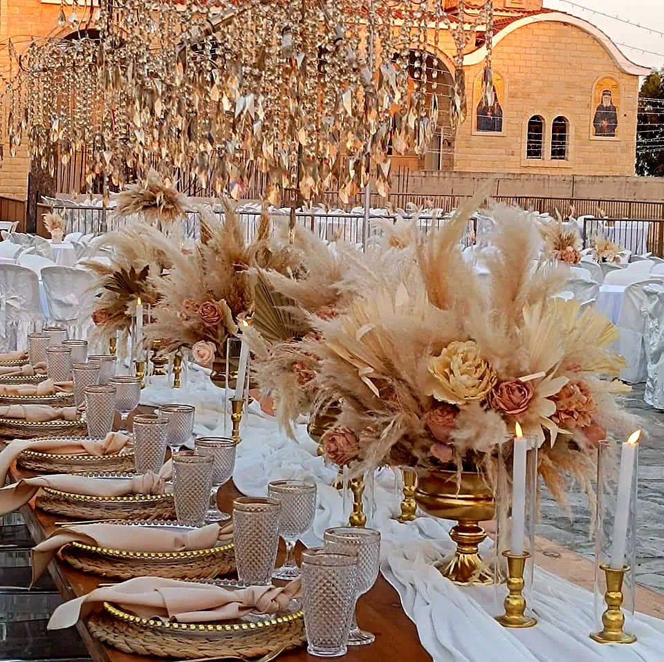 Reception tables with tall pampas grass arrangements and gold candelabra beside a stone church
