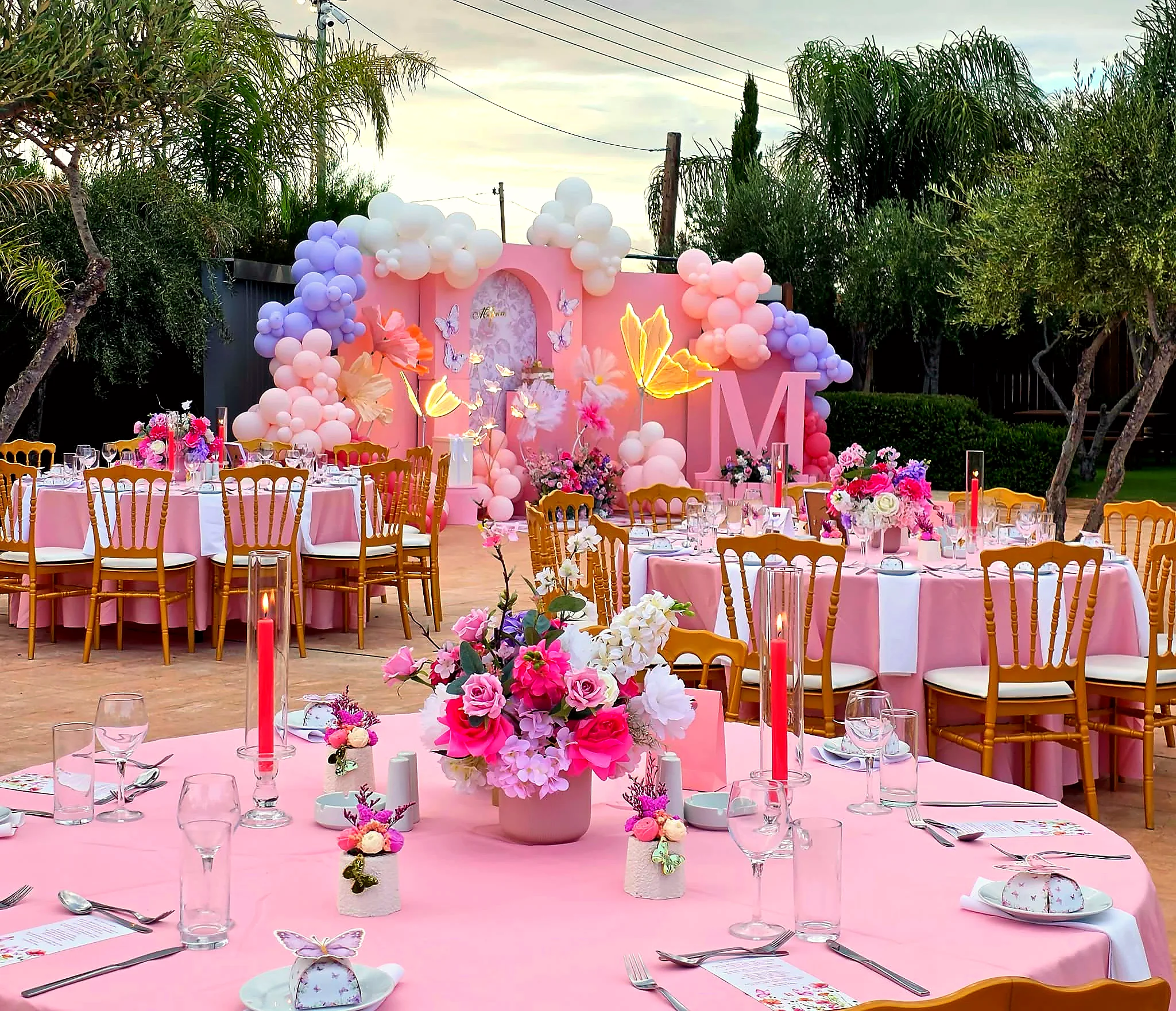 A pink celebration setting with balloon arches, paper butterflies and floral tables