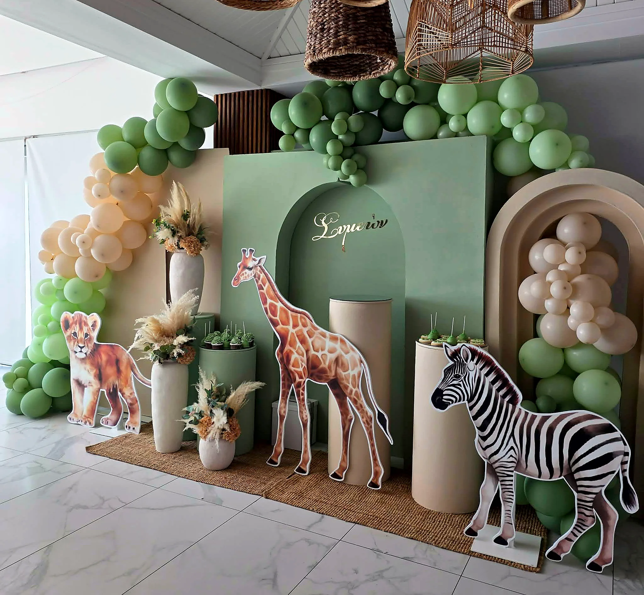 A green and gold safari-themed celebration backdrop with balloon garlands and animal figures