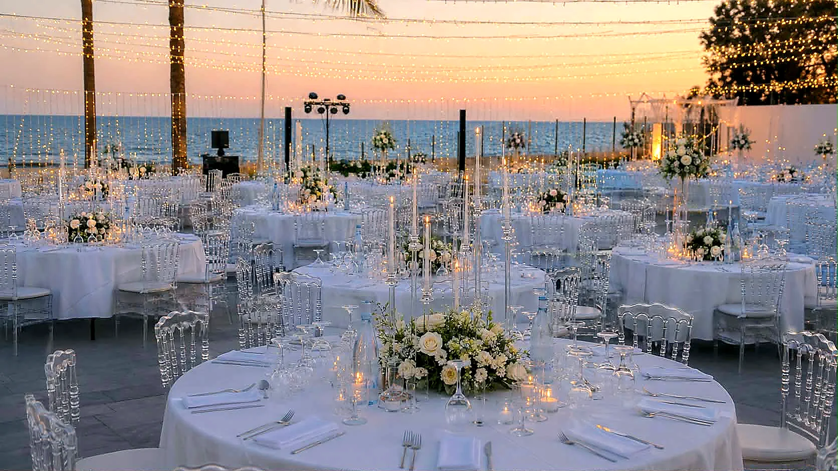 Reception tables laid in white beside the Mediterranean sea at sunset