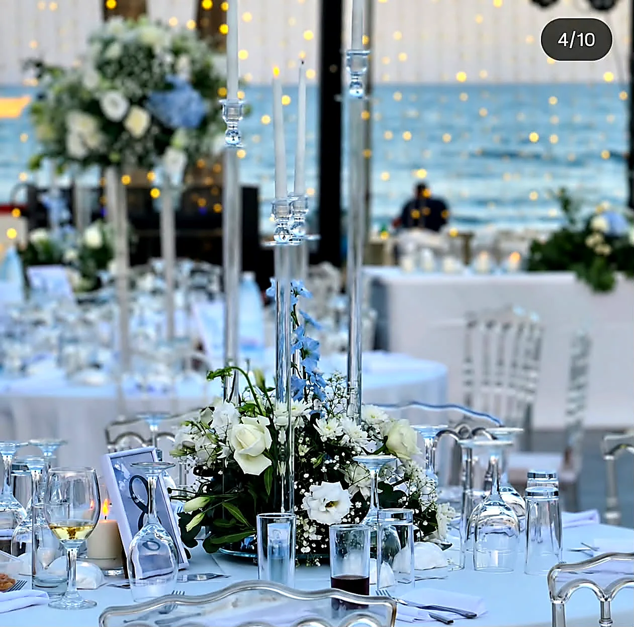 A tall glass centrepiece of white roses and hydrangeas on a reception table overlooking the sea
