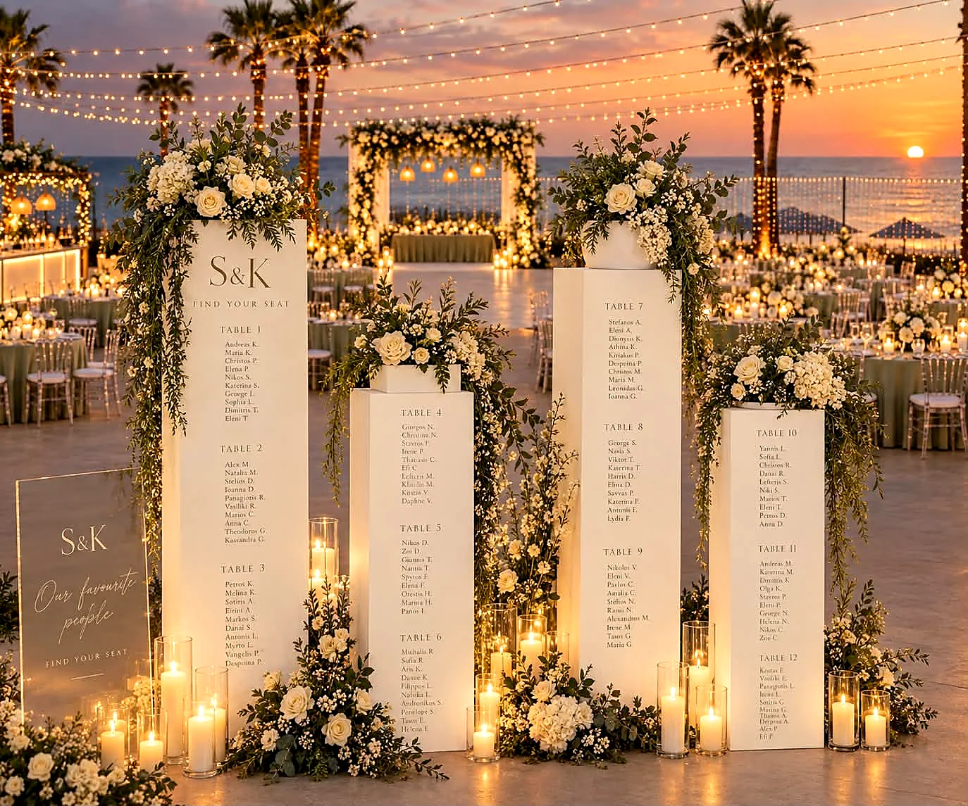 A seating plan displayed on floral-topped plinths at a seaside venue at sunset
