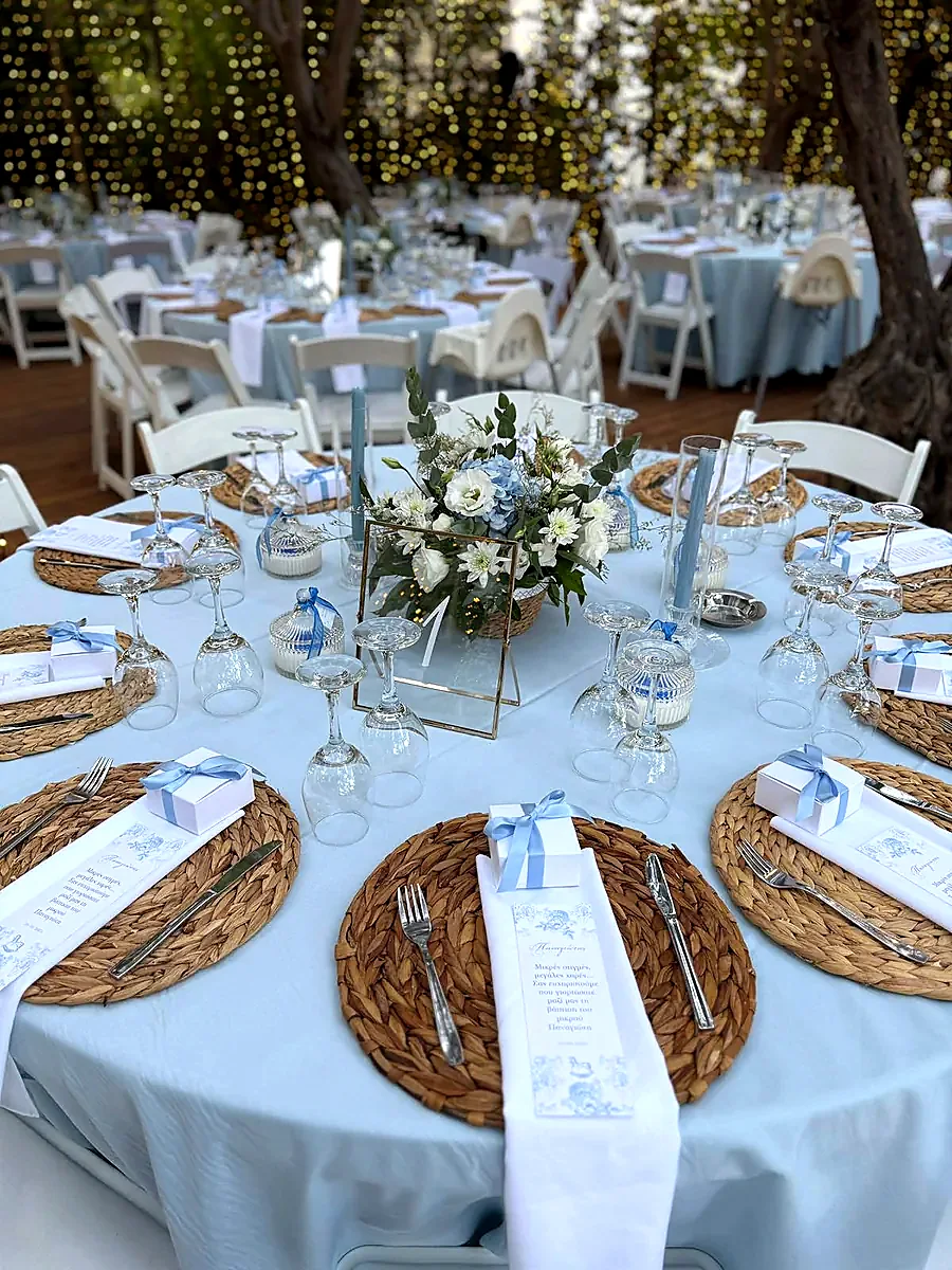 A round table laid with woven placemats, white florals and folded linen napkins